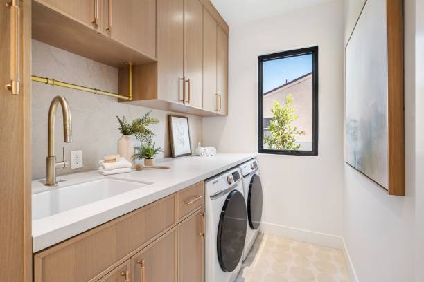 Modern laundry room with wooden cabinets, white countertops, and a window view, featuring a washer and dryer set.